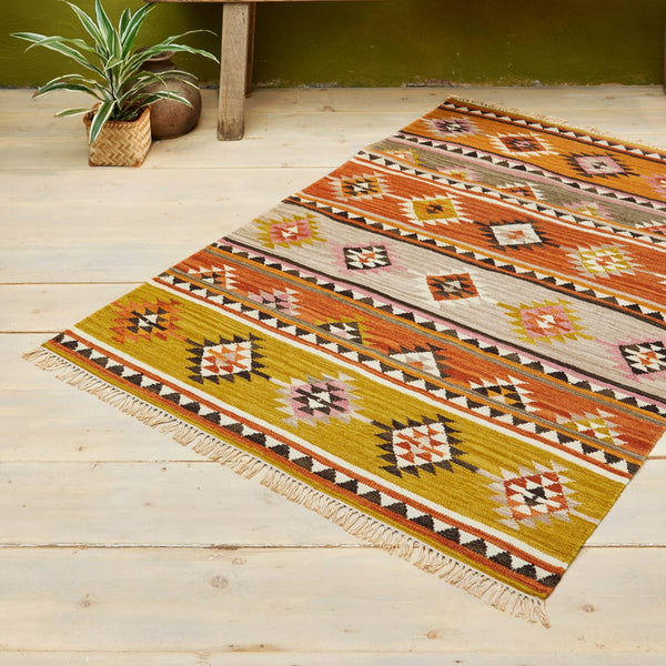 Decorative rug with geometric pattern on a wooden floor, accompanied by a wooden bench and decorative pillows.
