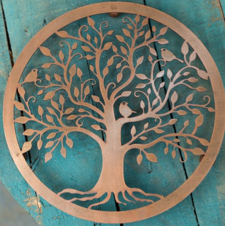 A bronze metal trivet with a tree of life design and birds perched on branches, placed on a blue surface.