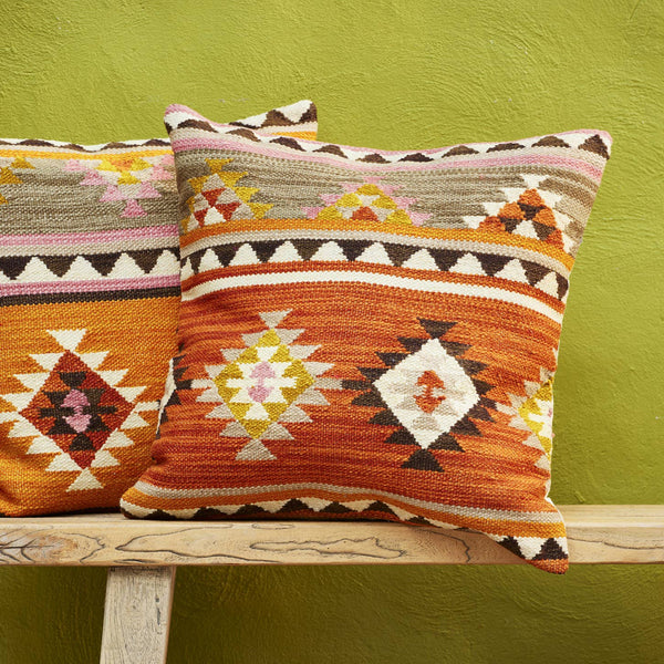 Two patterned pillows on a wooden bench against a green wall.