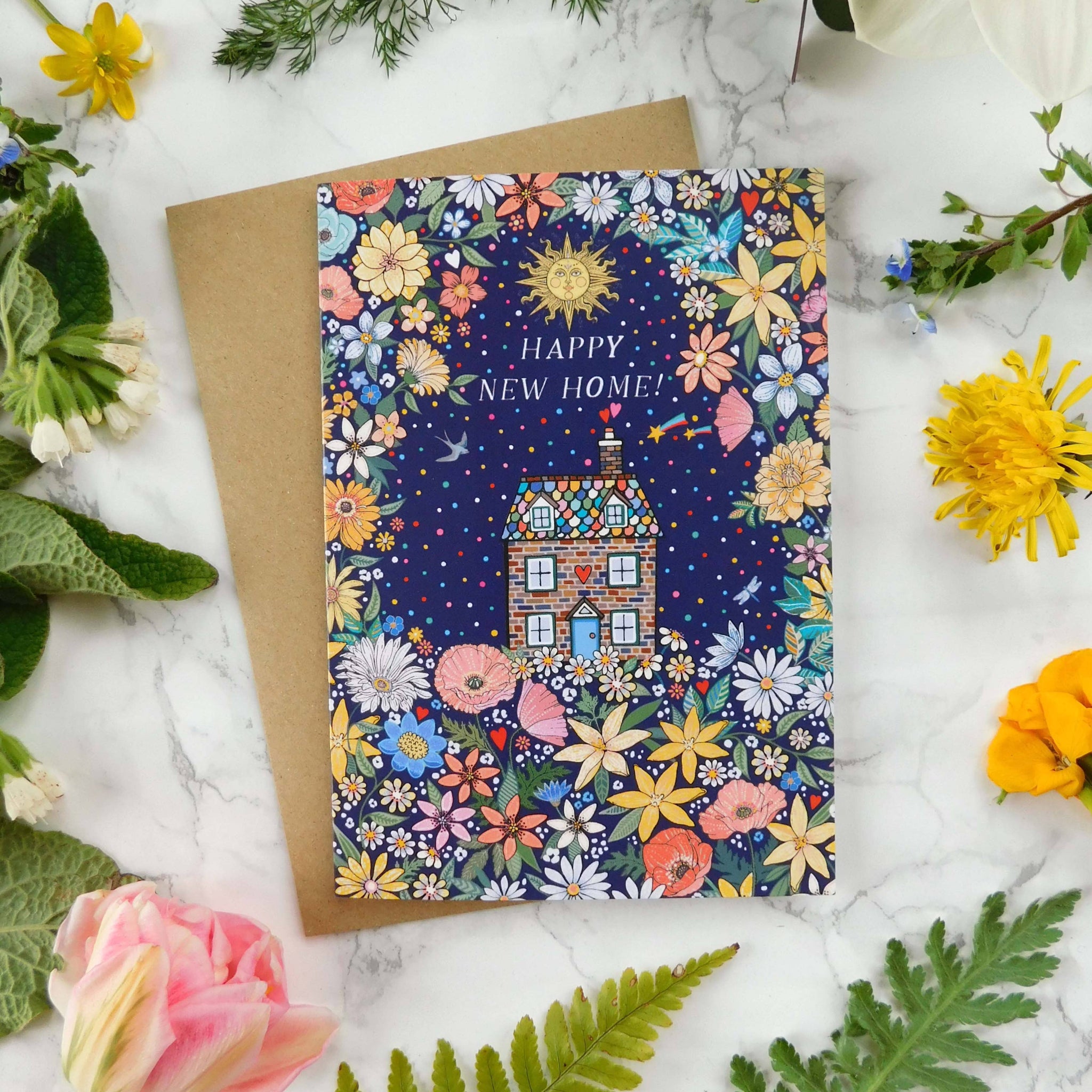 Greeting card with floral design and 'Happy New Home' text, surrounded by flowers and leaves on a marble surface.