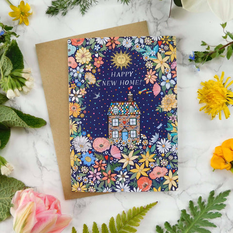 Greeting card with floral design and 'Happy New Home' text, surrounded by flowers and leaves on a marble surface.