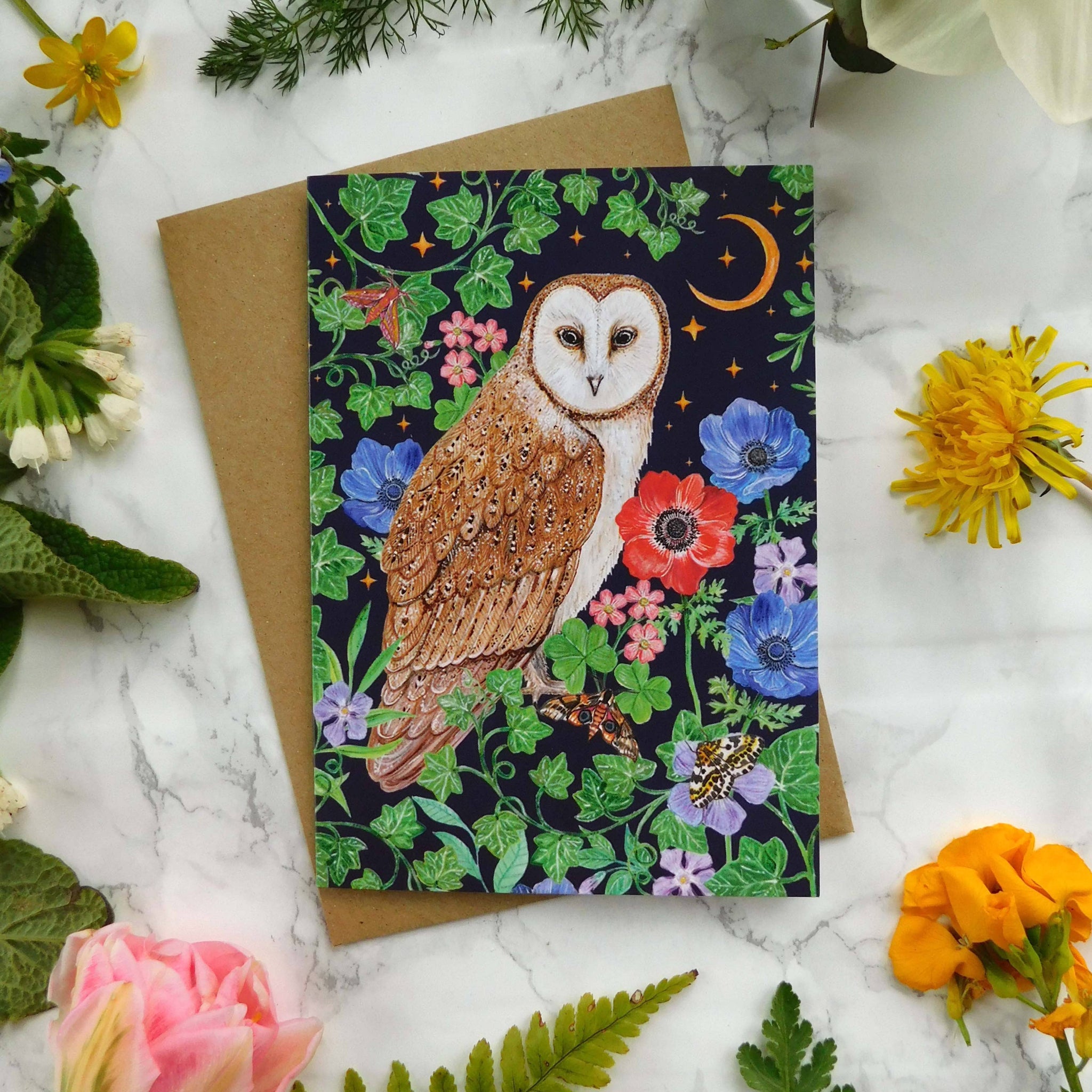 Greeting card with owl design surrounded by flowers and leaves on a marble surface