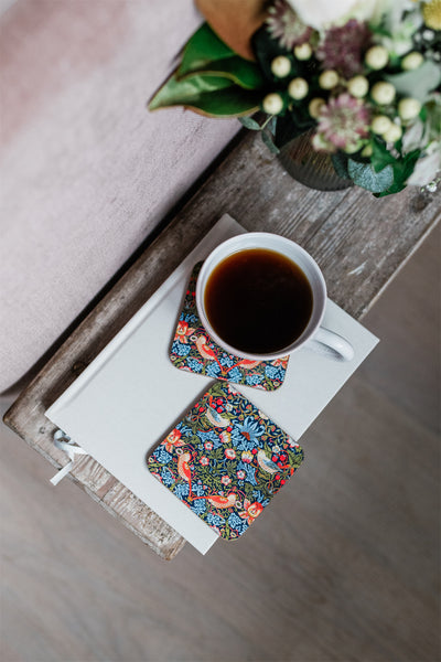 Cup of coffee with floral coasters on a notebook, with a bouquet of flowers in the background.