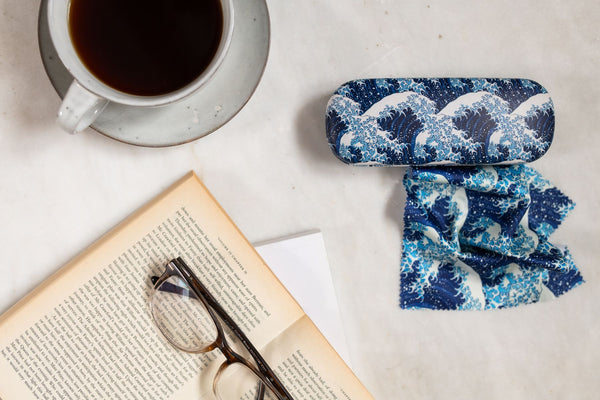 Glasses case with wave design next to an open book and cup of coffee on a light surface