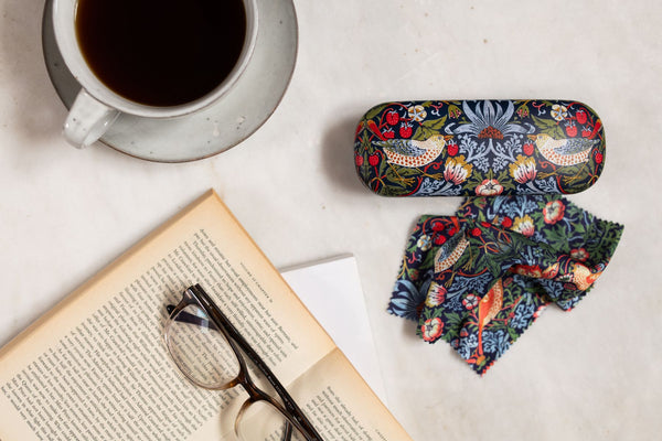 Colorful floral eyeglass case on a white surface with an open book and cup of coffee.