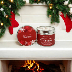 Christmas candle with red lid and festive decorations on a fireplace mantle.