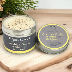 A tin of 'Arabian Oudh, Amber & Bergamot' scented candle on a wooden surface with a natural background.