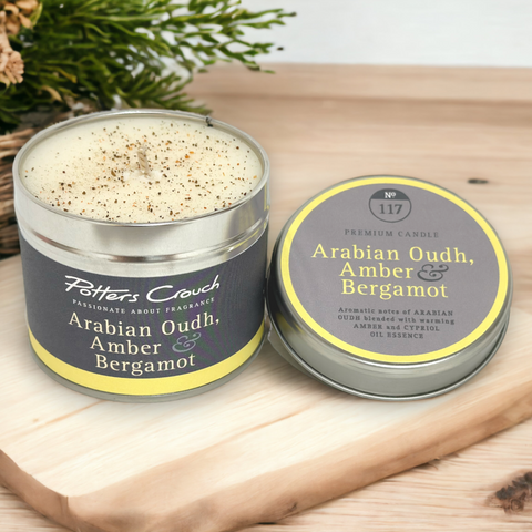 A tin of 'Arabian Oudh, Amber & Bergamot' scented candle on a wooden surface with a natural background.