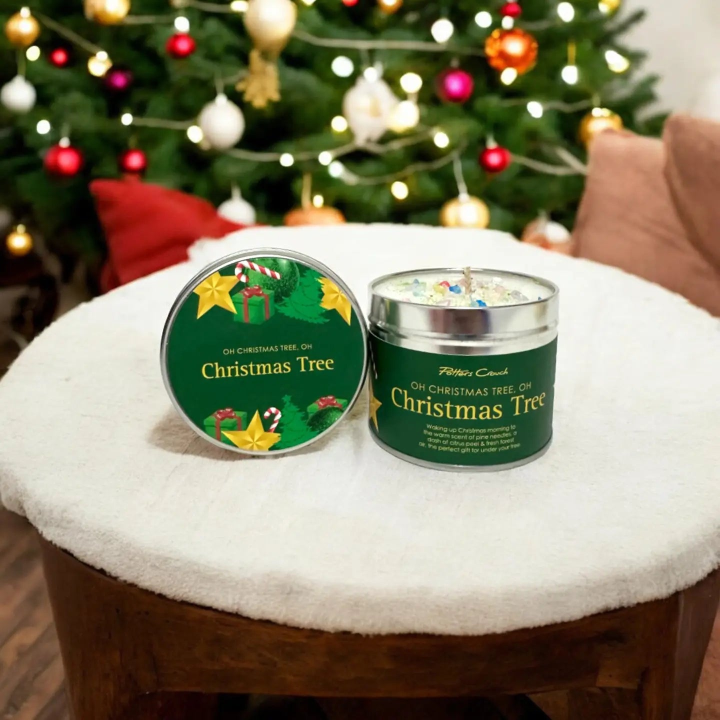 Two candles labeled 'Oh Christmas Tree' on a cushioned stool with a decorated Christmas tree in the background.