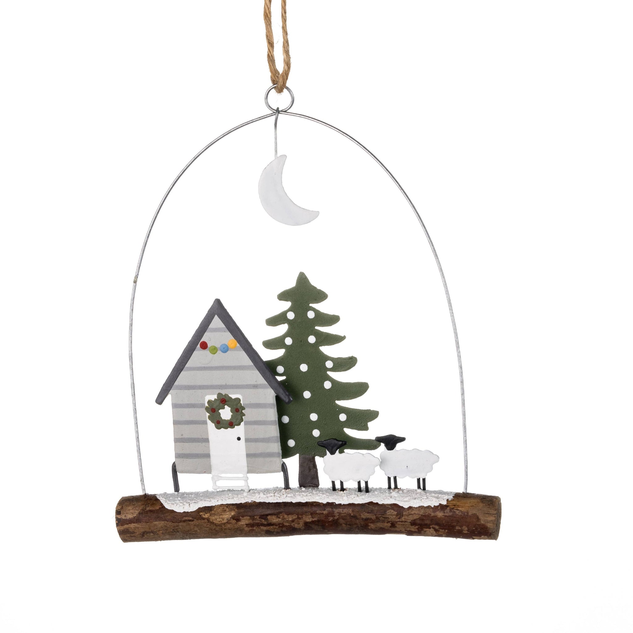 Decorative hanging ornament with a cabin, tree, and sheep on a white background