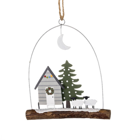 Decorative hanging ornament with a cabin, tree, and sheep on a white background