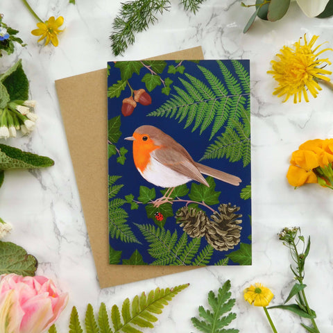 Card with a robin design surrounded by flowers and leaves on a marble surface