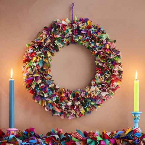 Colorful fabric wreath and garland on a wooden surface with candles.