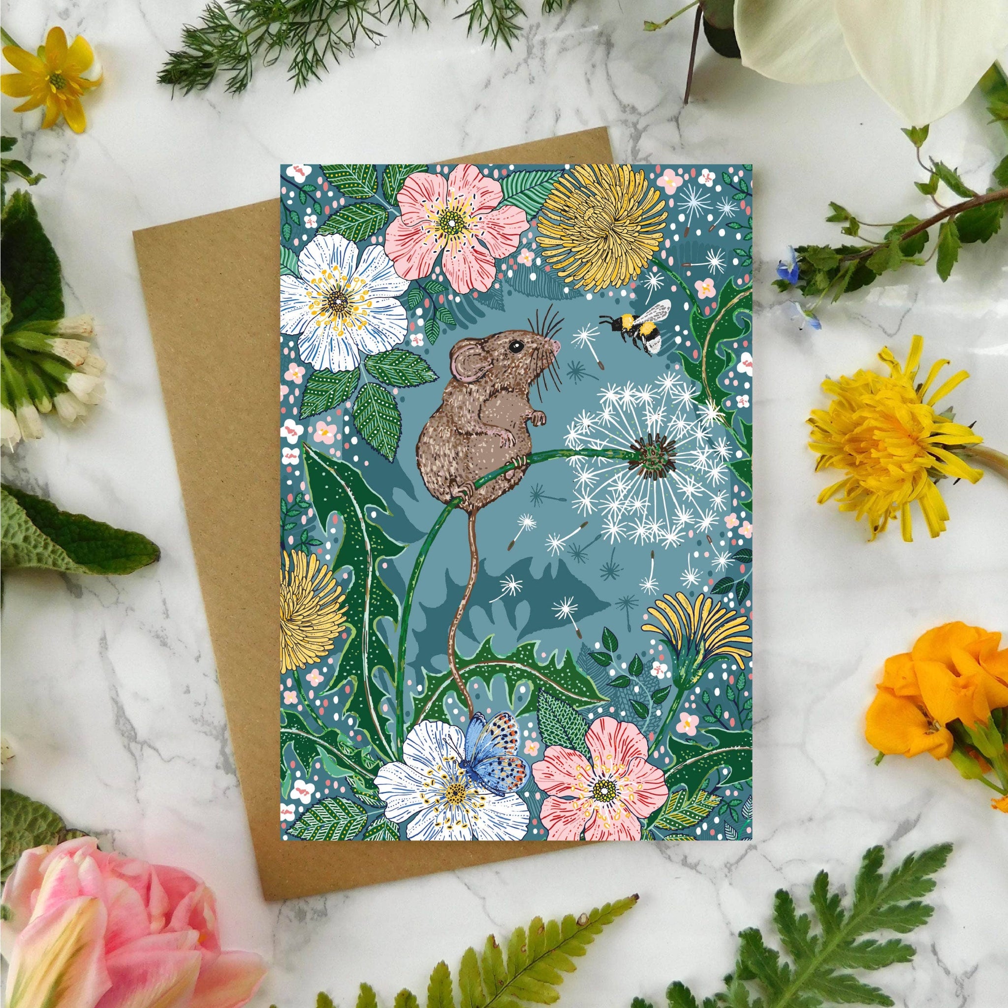 Greeting card with mouse illustration surrounded by flowers and plants on a marble surface