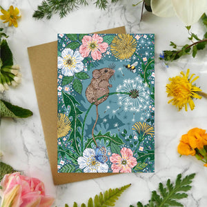 Greeting card with mouse illustration surrounded by flowers and plants on a marble surface