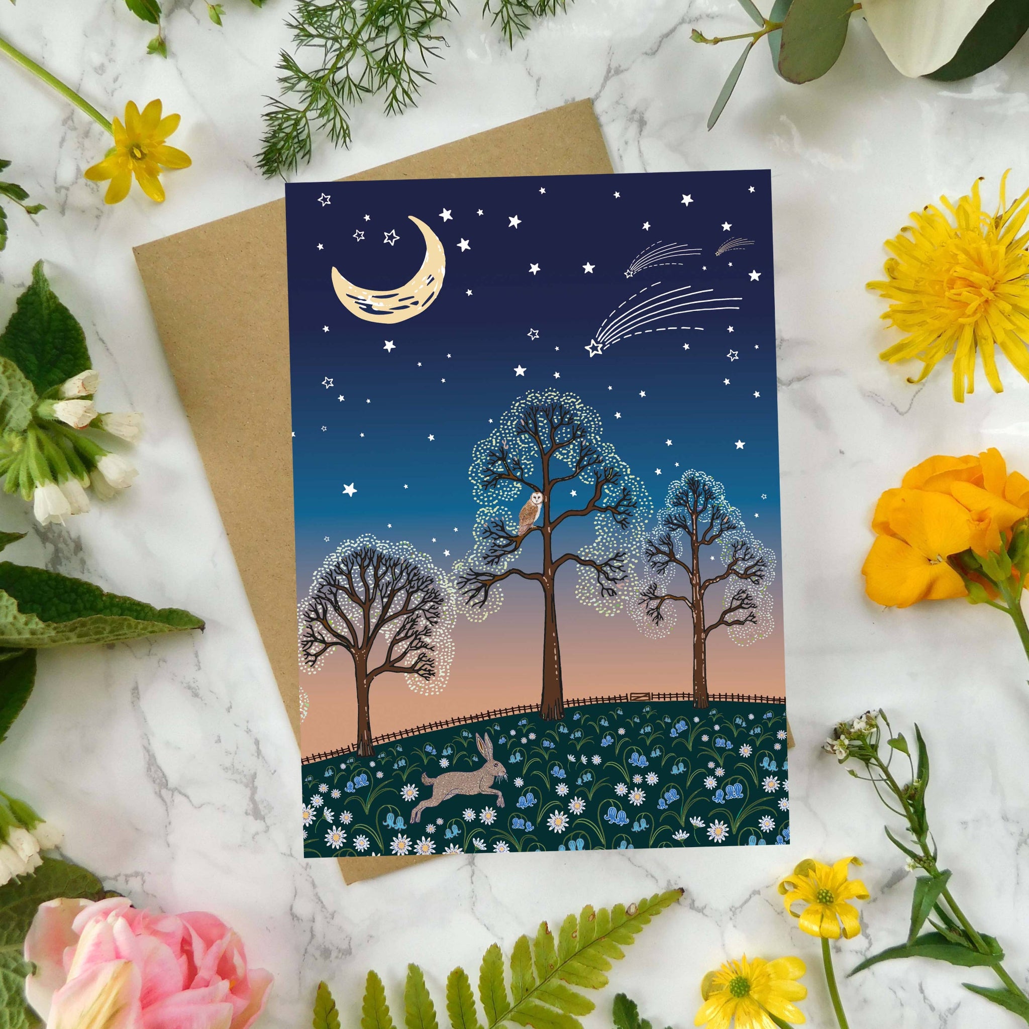 Greeting card with nature-themed design surrounded by flowers and leaves on a marble surface