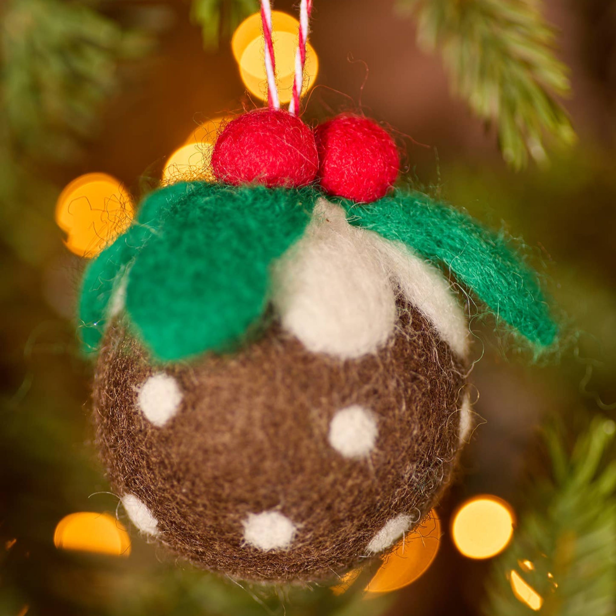 Felted Christmas pudding ornament on a tree with blurred lights in the background