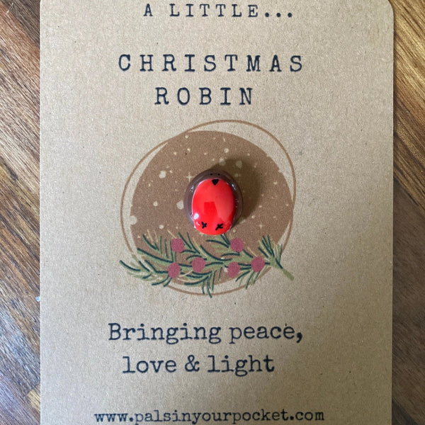 Red Christmas robin pin on a brown card with text on a wooden surface