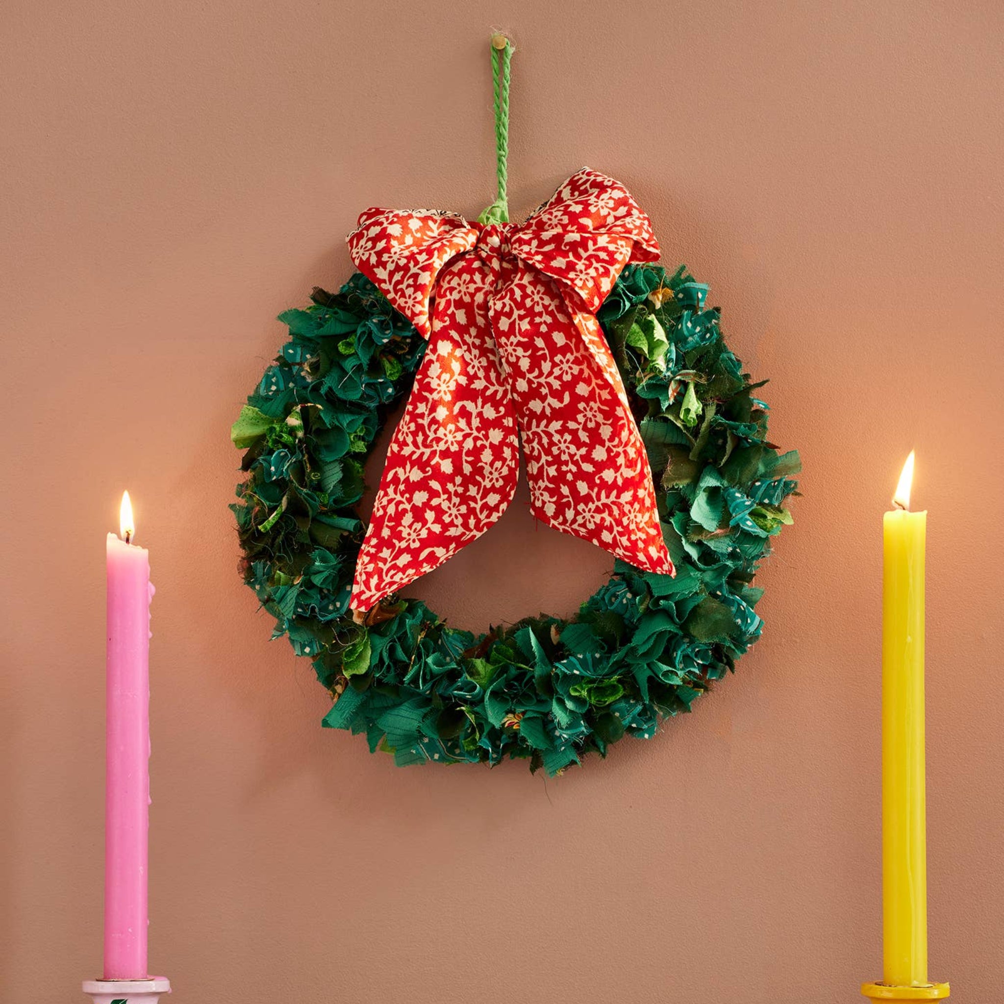 Christmas wreath with a red bow, candles, and garland on a wooden surface.