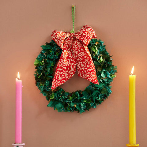 Christmas wreath with a red bow, candles, and garland on a wooden surface.