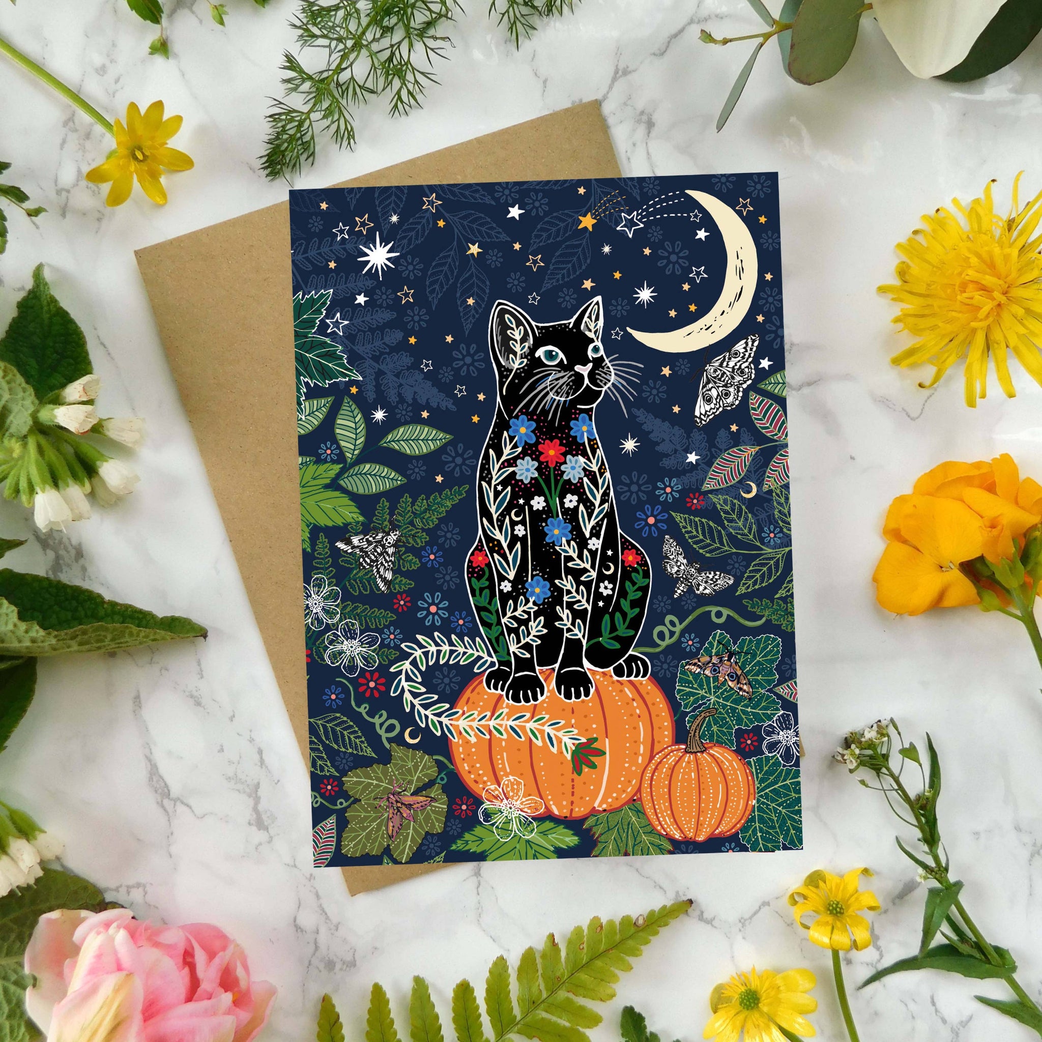 Greeting card with a cat design surrounded by flowers and leaves on a marble surface