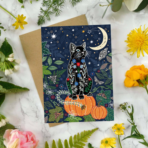 Greeting card with a cat design surrounded by flowers and leaves on a marble surface