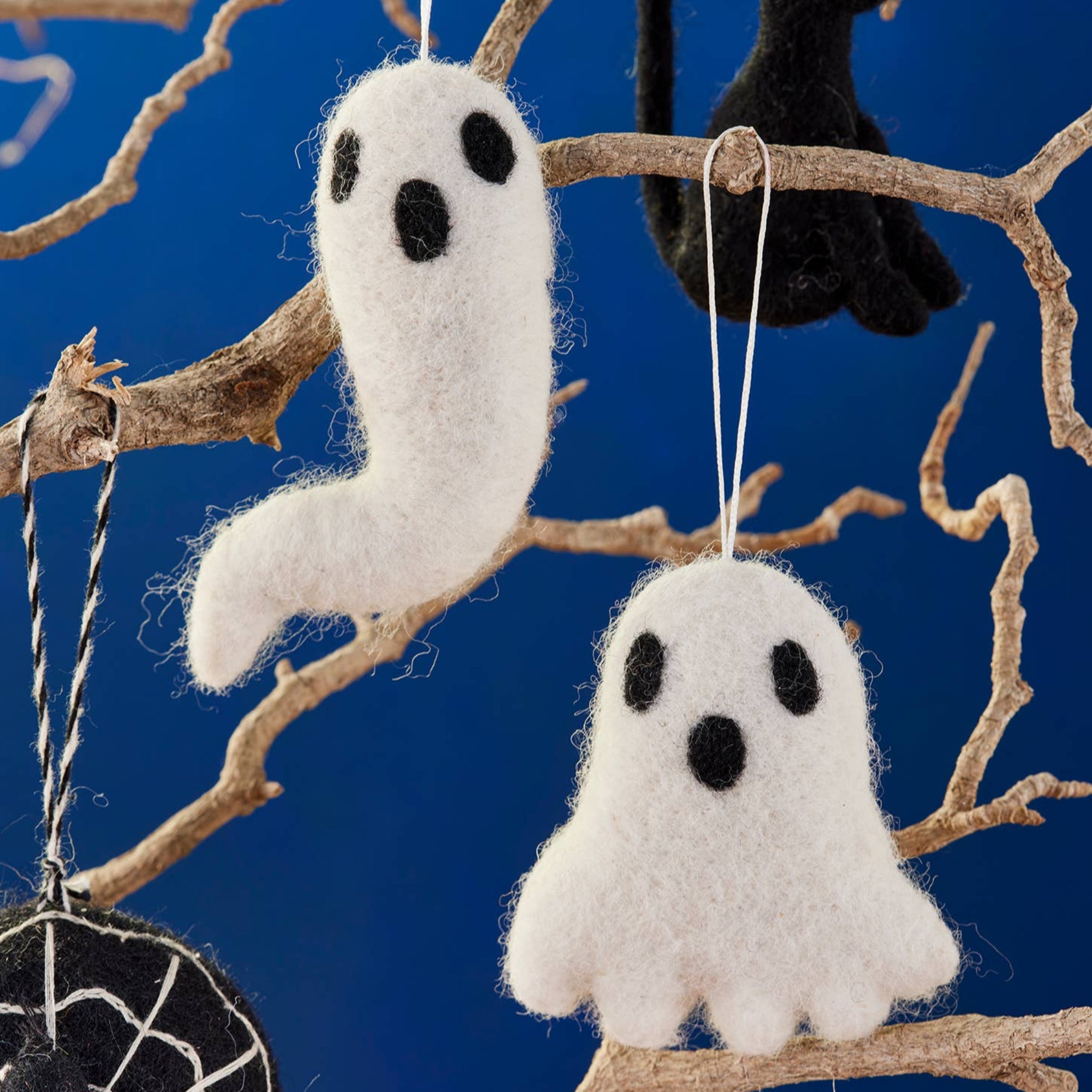 Halloween-themed decorations including white ghosts, a black cat, and a spider web on a branch against a blue background.