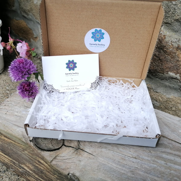 Open cardboard box with decorative paper and a business card on a stone surface with flowers and a plant.