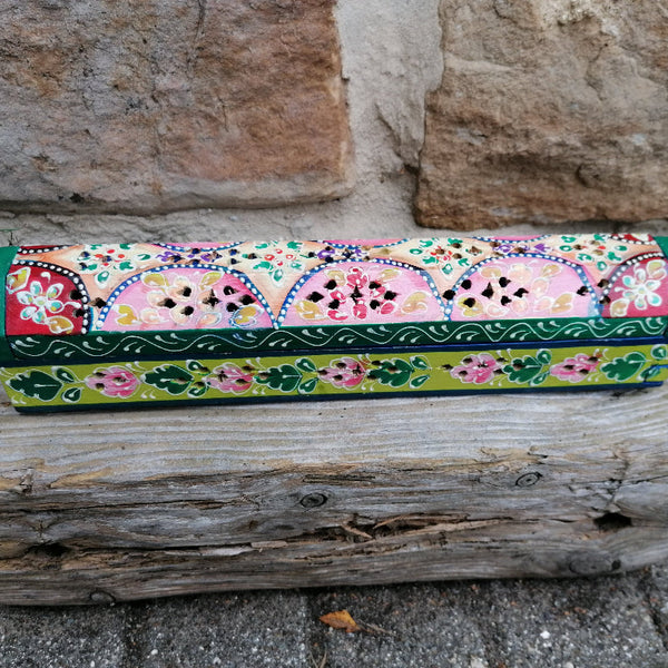 Colorful hand-painted box on a wooden log with stone wall background