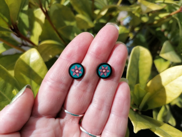 Pair of floral stud earrings held between fingers with a green leafy background