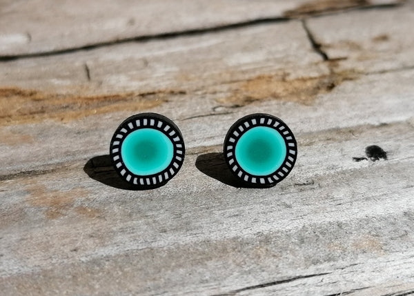 Turquoise earrings with black borders on a wooden surface