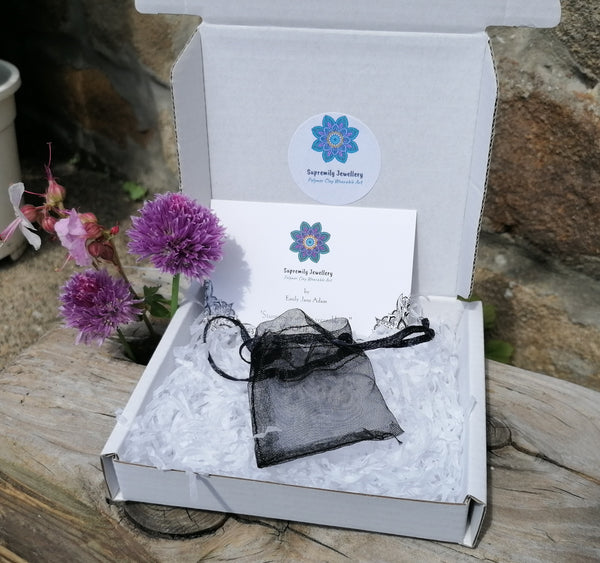 Jewelry box with a black jewelry bag and card on a wooden surface with flowers.