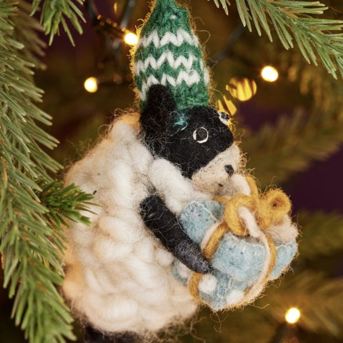 Felted animal ornament hanging on a Christmas tree with greenery and lights in the background.