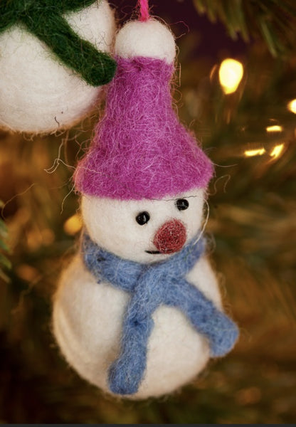 Felted snowman ornament with a purple hat and blue scarf on a blurred Christmas tree background.
