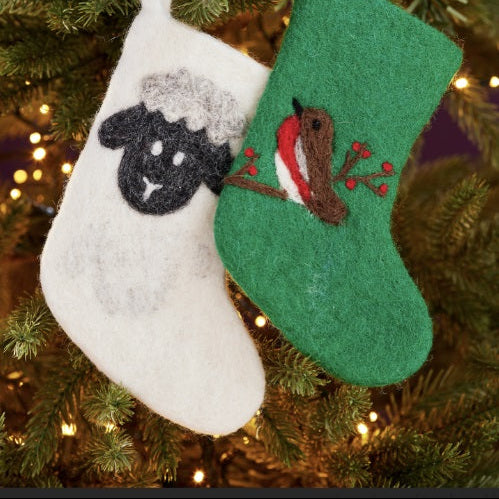 Two Christmas stockings, one white with a black sheep design and one green with a brown horse design, hanging on a decorated tree.