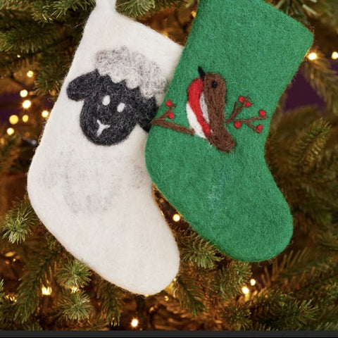Two Christmas stockings, one white with a black sheep design and one green with a brown horse design, hanging on a decorated tree.