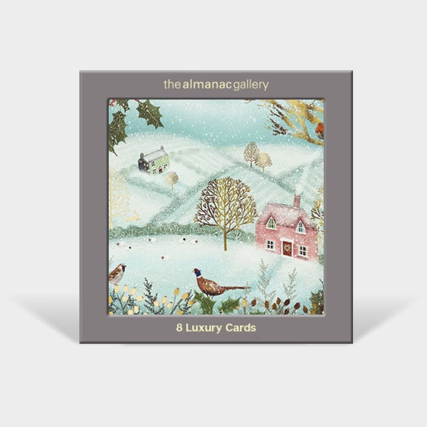 A square boxed card set titled 'the almanac gallery' with '8 Luxury Cards' printed below the illustration. The front shows a winter landscape painting with snow, a pink house, birds, and trees, set against a light gray background.
