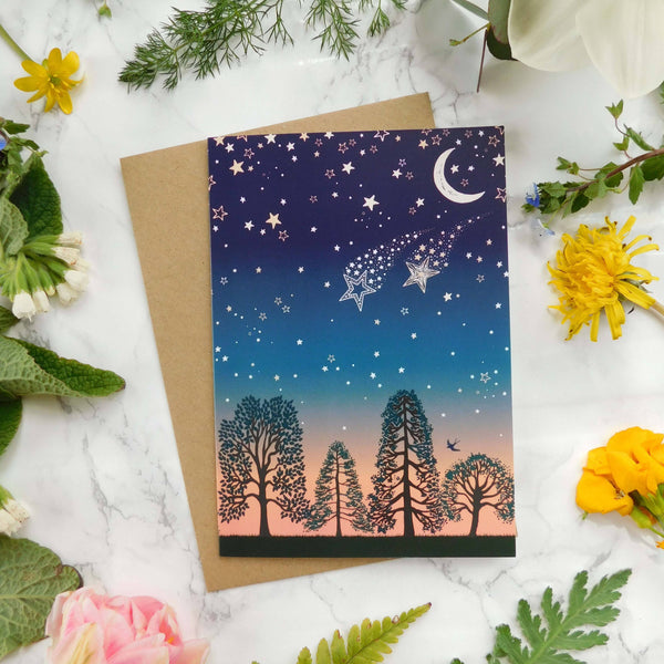 Greeting card with starry night design surrounded by flowers and leaves on a marble surface