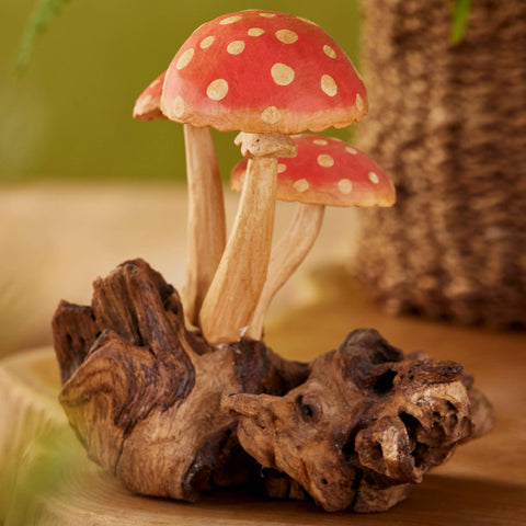 Decorative mushrooms with red caps and white spots on a wooden base against a green background
