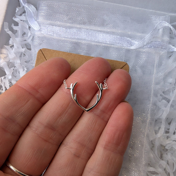 Silver heart-shaped earring held between fingers against a white box background