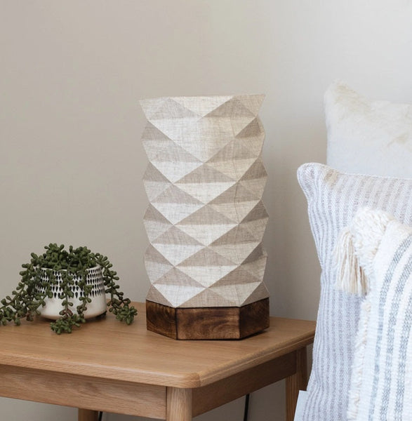 Geometric-patterned lamp on a wooden nightstand next to a bed with pillows