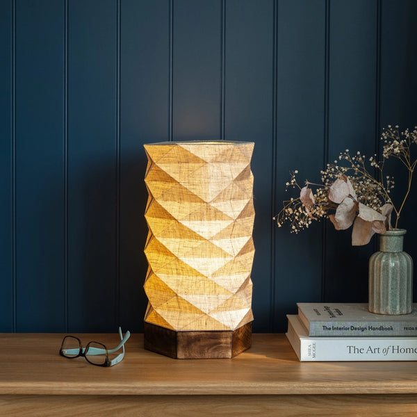 Geometric-patterned lamp on a wooden surface with a dark blue wall background