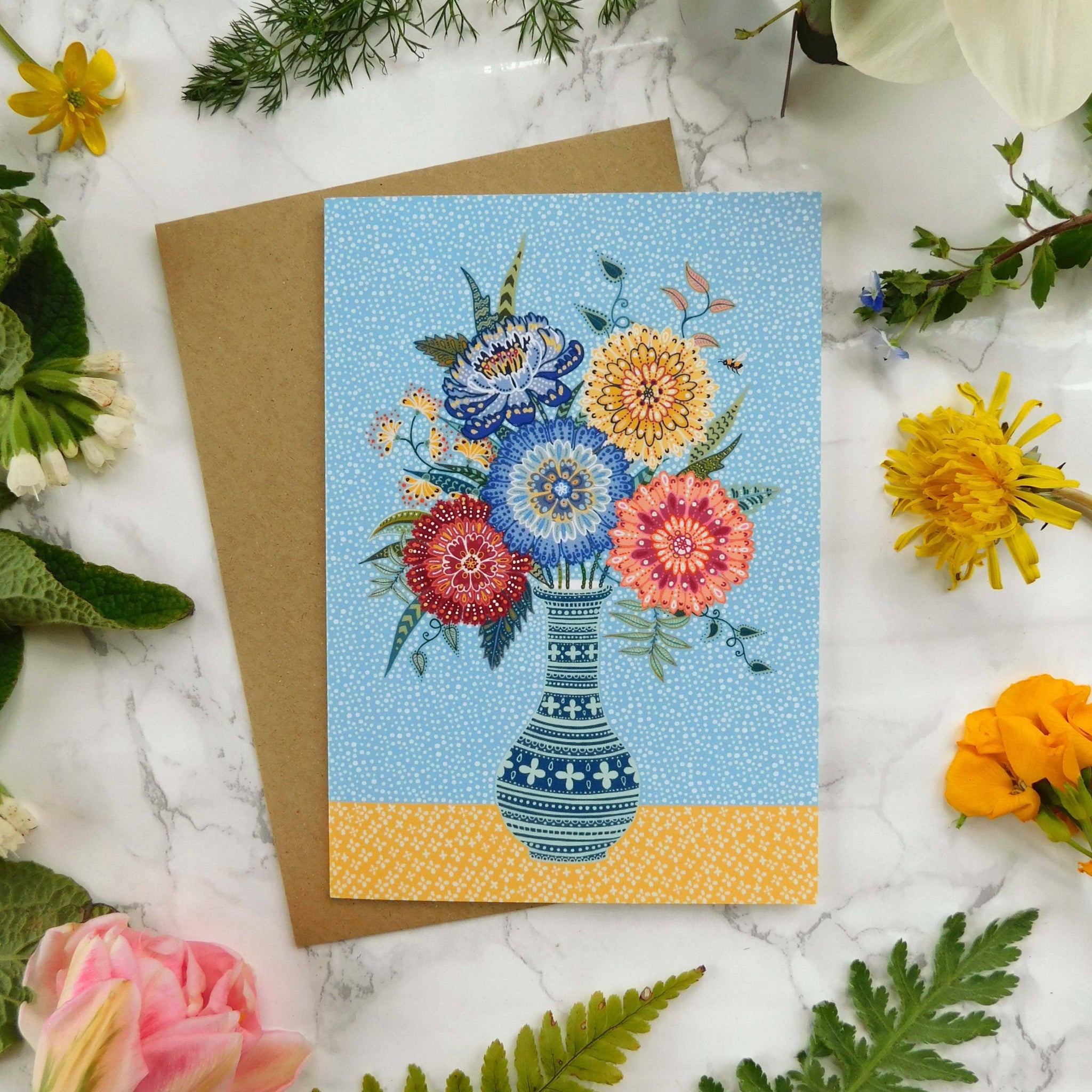 Greeting card with floral design on a marble surface surrounded by flowers and leaves