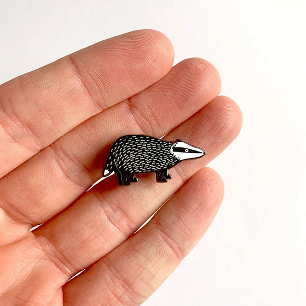 Small black and white badger-shaped pin held between fingers on a white background