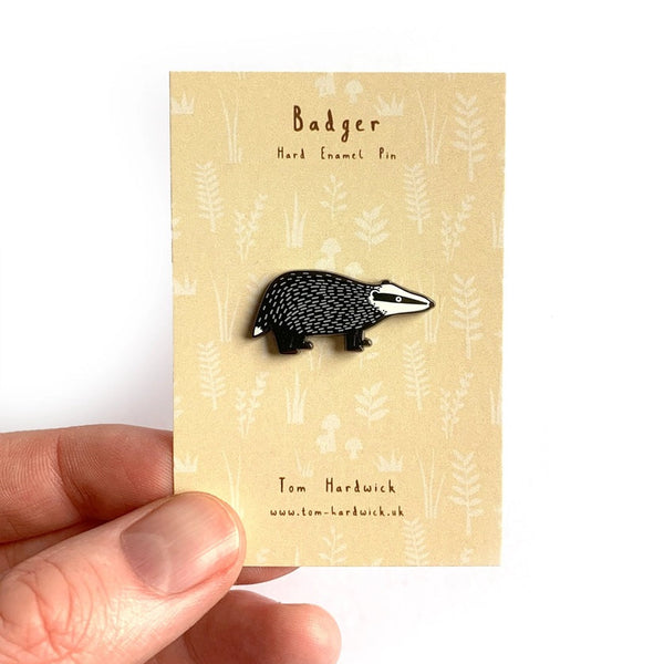 Badger enamel pin on a decorative card held by a hand