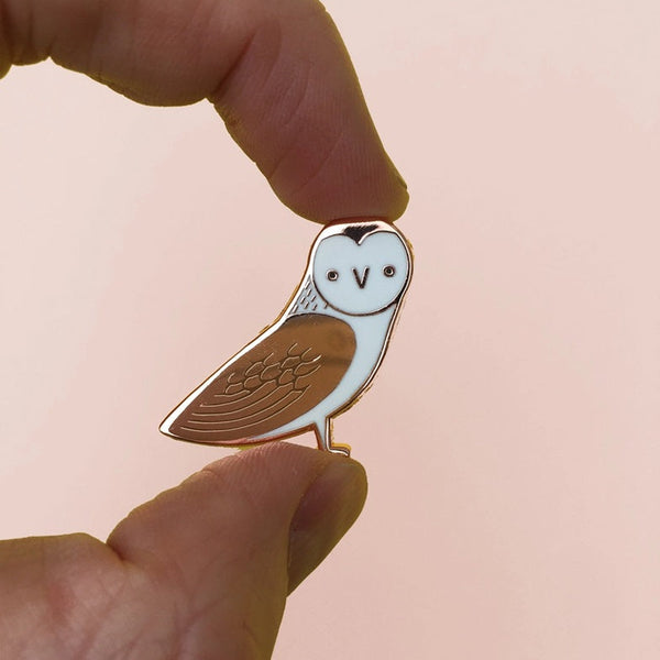 Hand holding a small owl-shaped pin against a plain background