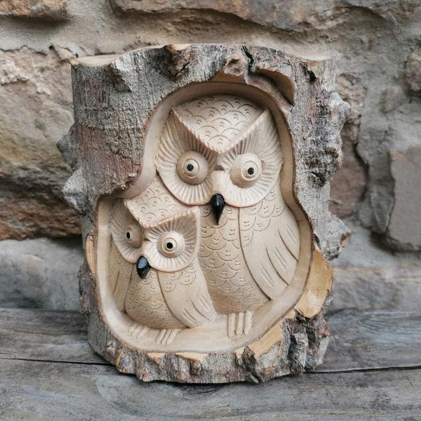 Wooden owl carvings inside a natural wooden log against a stone wall background