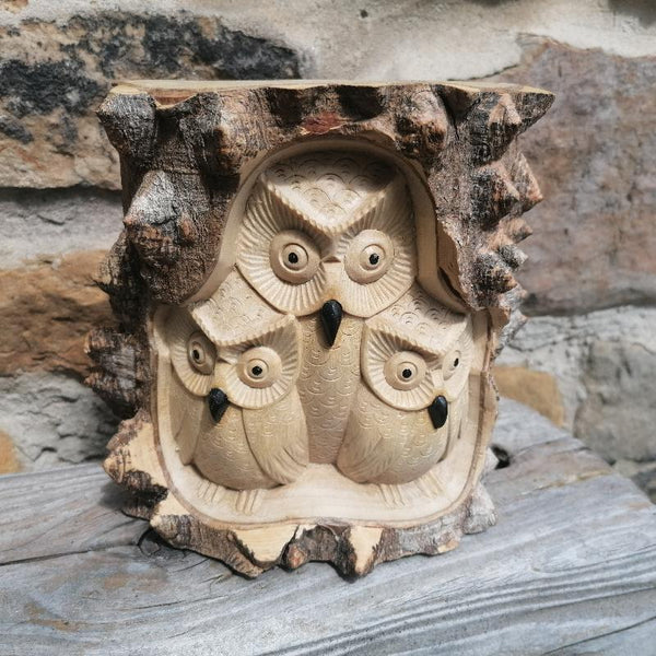 Wooden sculpture of three owls on a natural stone background