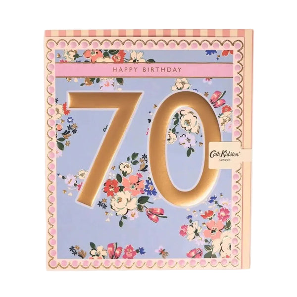 A square 70th birthday card by Cath Kidston, featuring a pastel lavender background with a pink and peach scalloped border, a floral print, and large gold '70' numerals. A small Cath Kidston tag is attached on the right side.