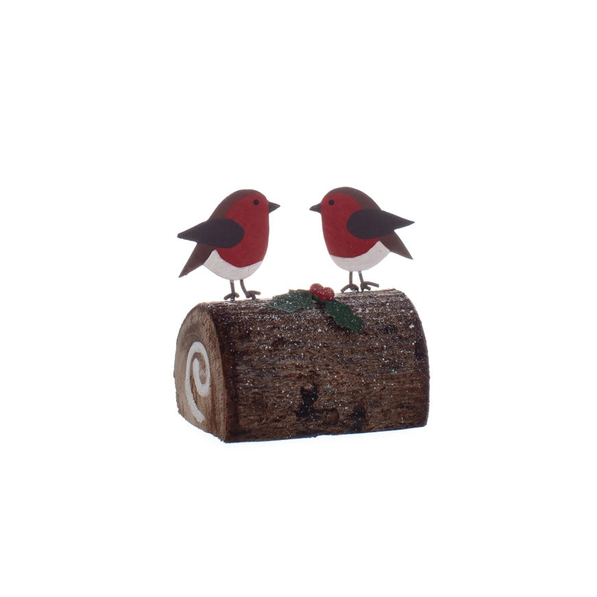 Two robin bird figurines on a log with holly leaves and berries against a white background